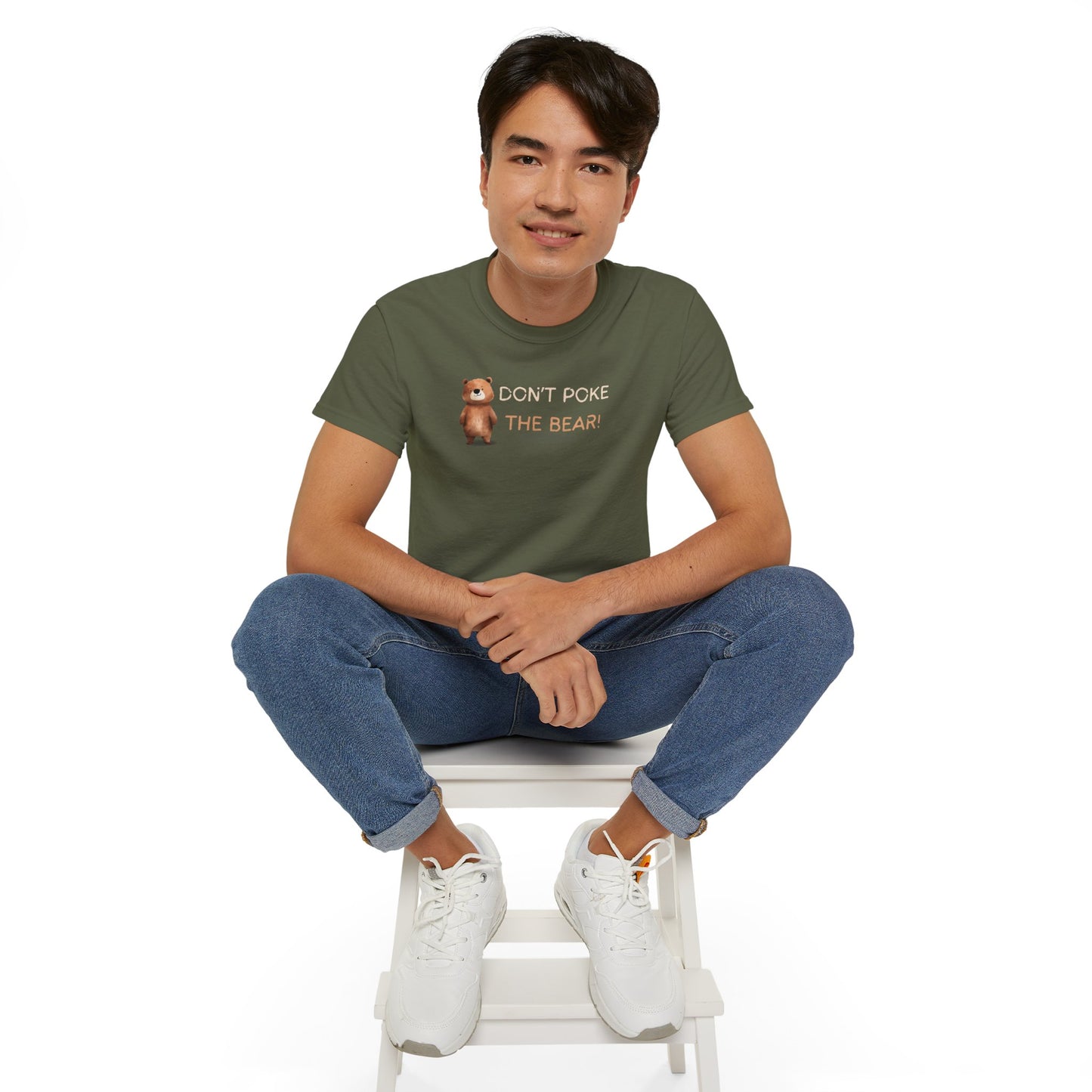 Person wearing a green t-shirt with text and graphics, sitting on a white stool against a white background