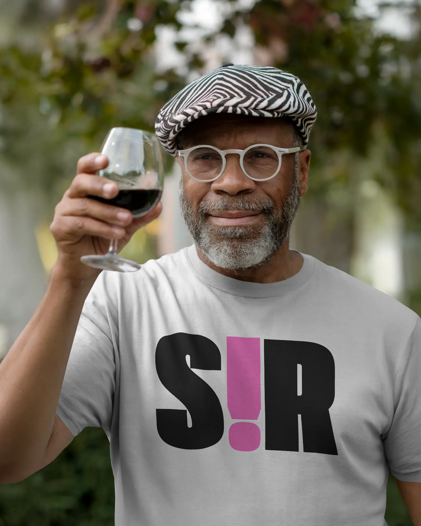 Man holding a glass of red wine outdoors wearing a t-shirt with 'S!R' design. Kink, LGBTQIA+, Queer Sub Dom