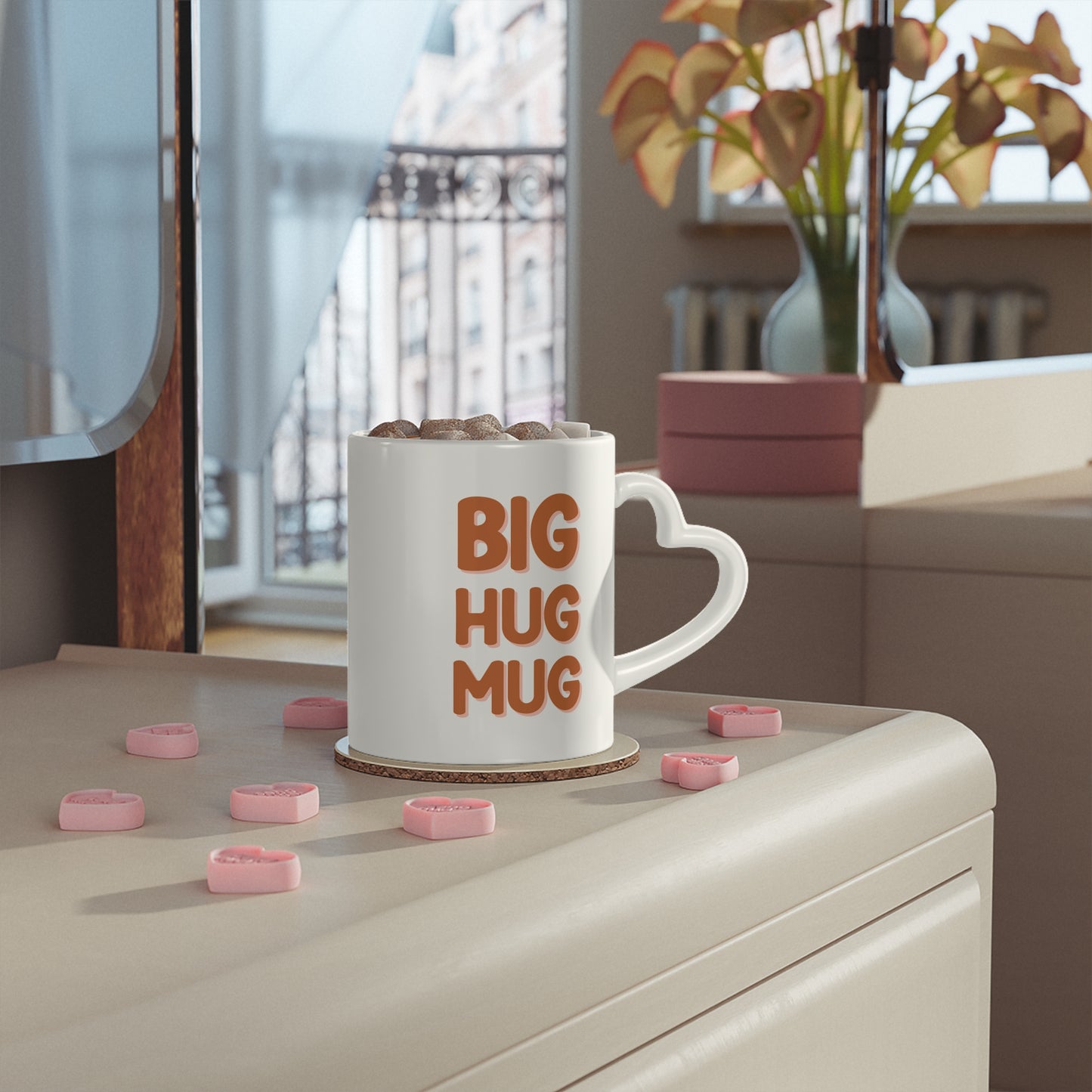 White mug with 'BIG HUG MUG' text on a surface with pink heart-shaped objects.