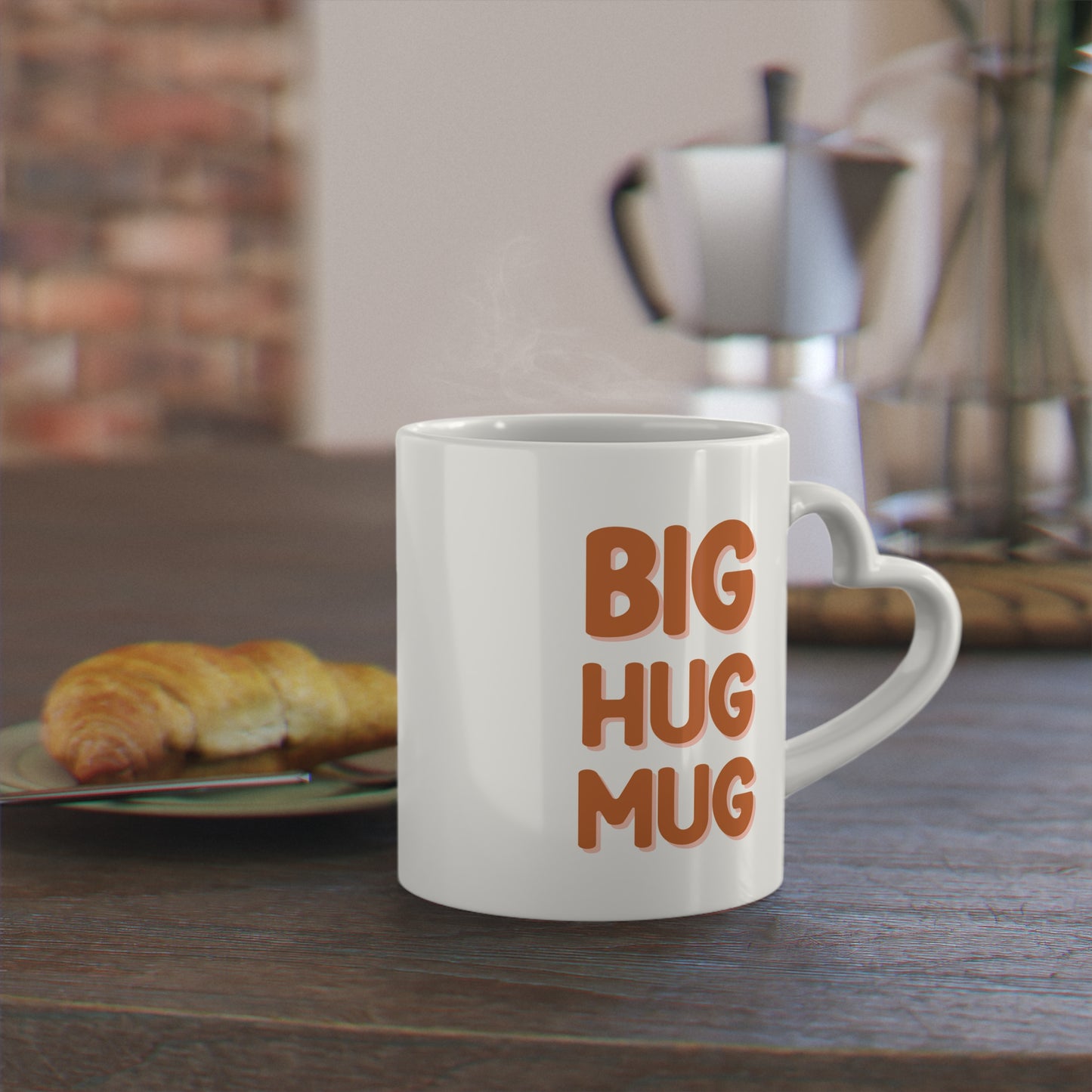 White mug with 'BIG HUG MUG' text on a wooden table with a croissant and coffee press in the background.