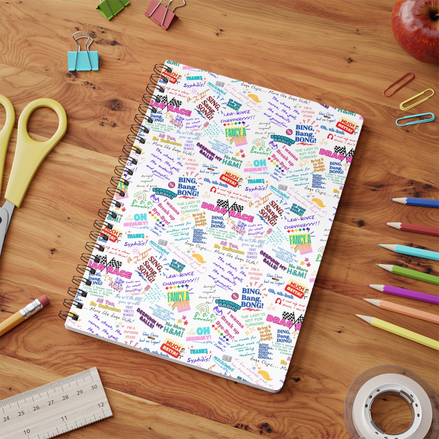 Notebook with colorful text design on a wooden surface with stationery items. features Iconic Quotes from Rupaul's Drag Race drag queens.