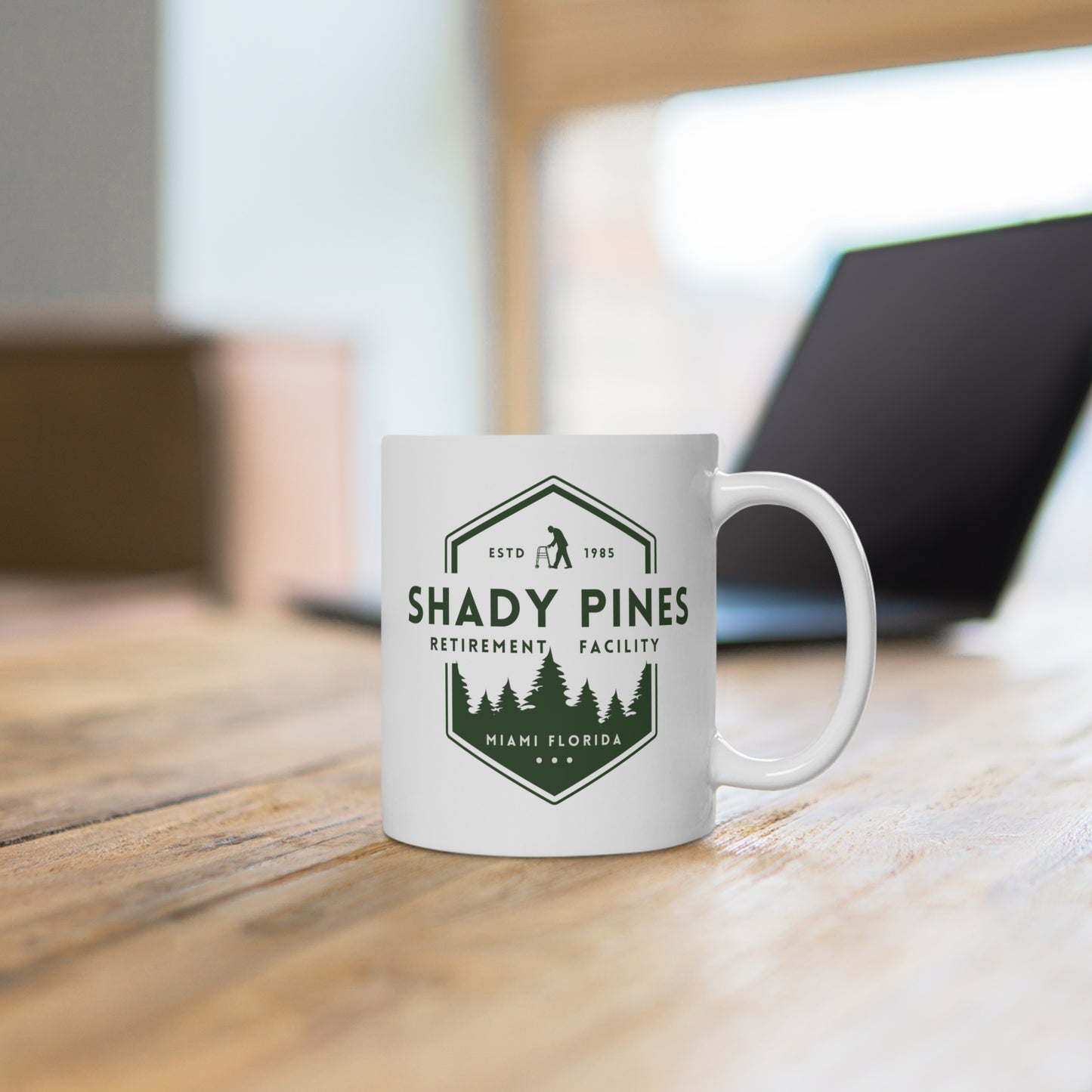 White mug with 'Shady Pines Retirement Facility' design on a wooden surface.