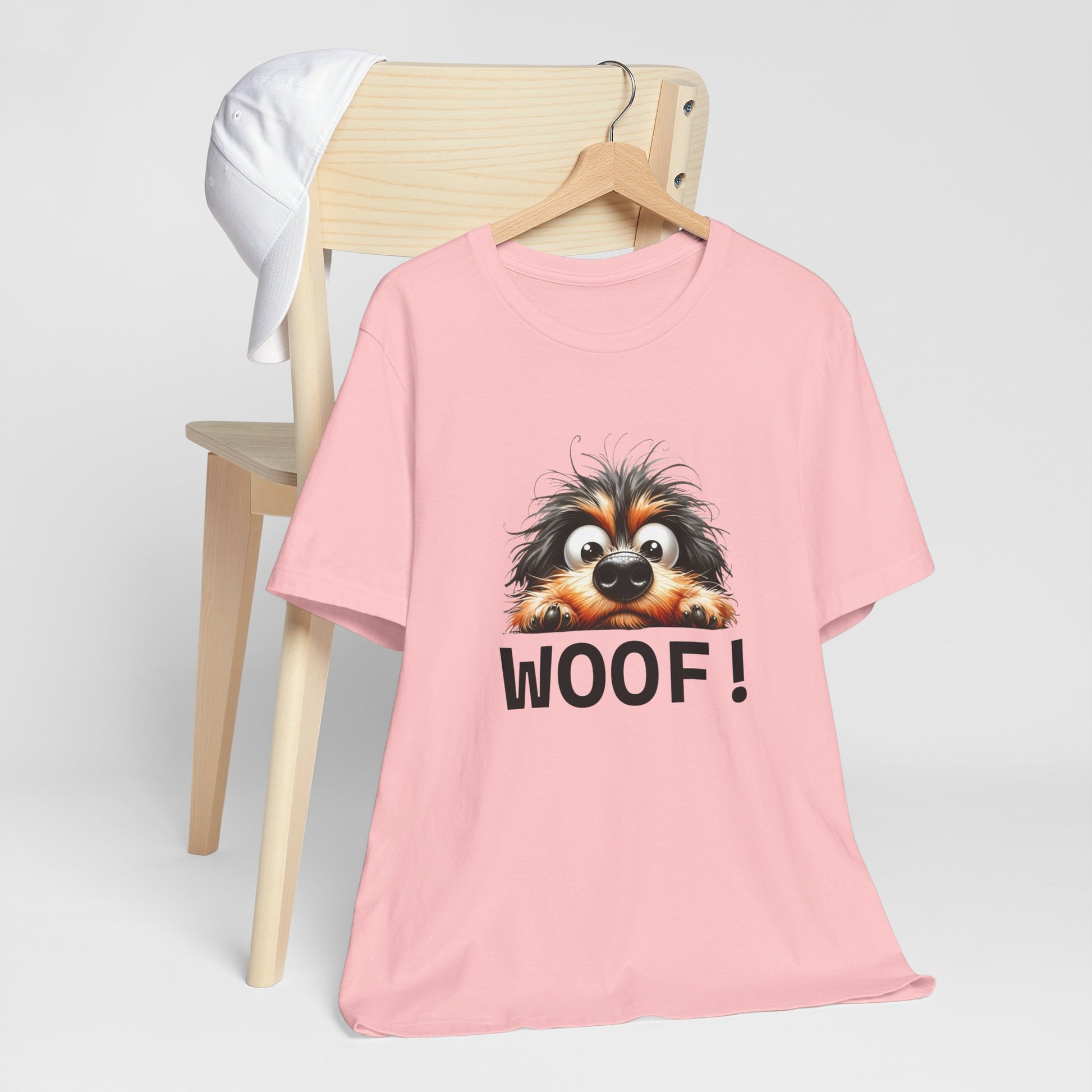 Pink t-shirt with a dog graphic and 'WOOF!' text on a chair against a white background