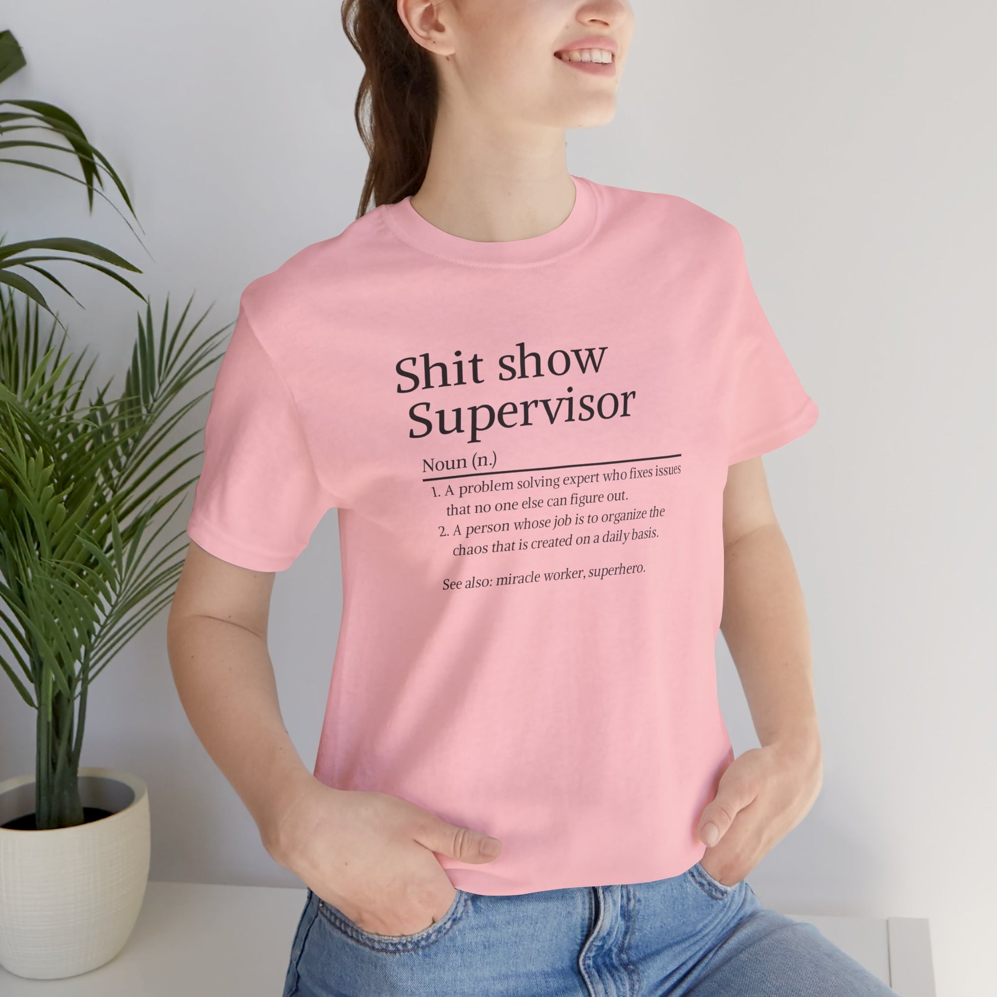 Person wearing a pink t-shirt with text design, sitting indoors with a plant in the background.