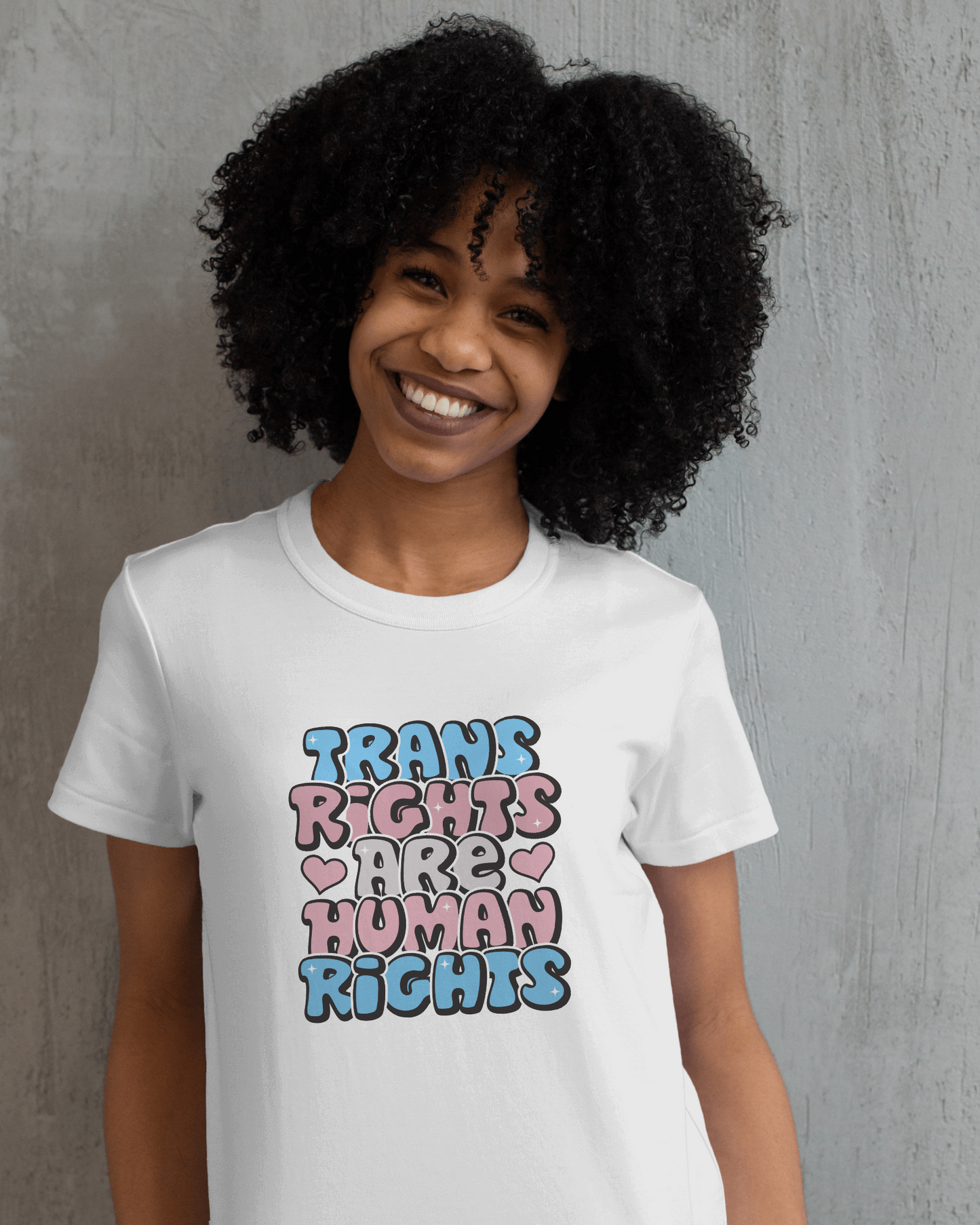 Person wearing a white t-shirt with 'Trans Rights Are Human Rights' text in colorful letters against a gray background. LGBTQIA+, Queer, Trans rights
