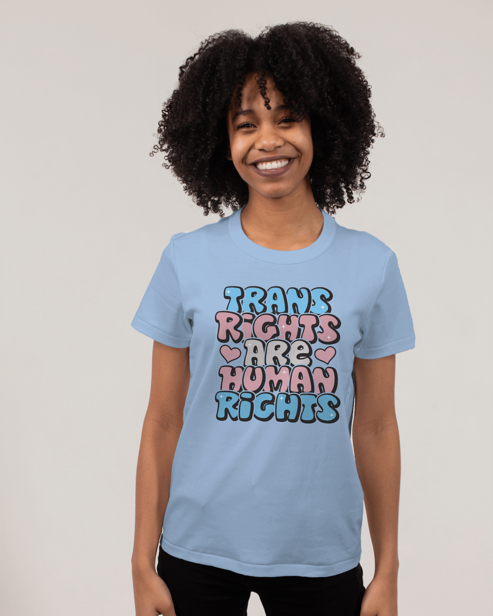 Person wearing a light blue t-shirt with colorful text on a plain background LGBTQIA+, Queer, Trans rights