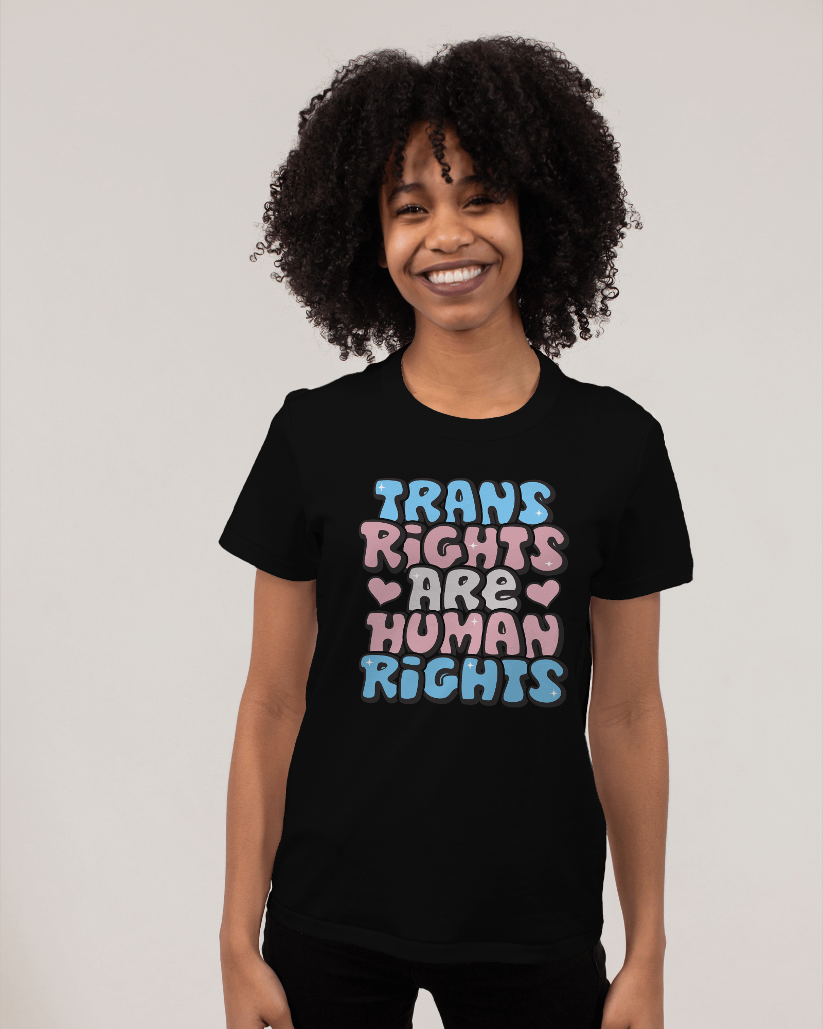 Person wearing a black t-shirt with 'Trans Rights Are Human Rights' text in colorful letters on a plain background LGBTQIA+, Queer, Trans rights