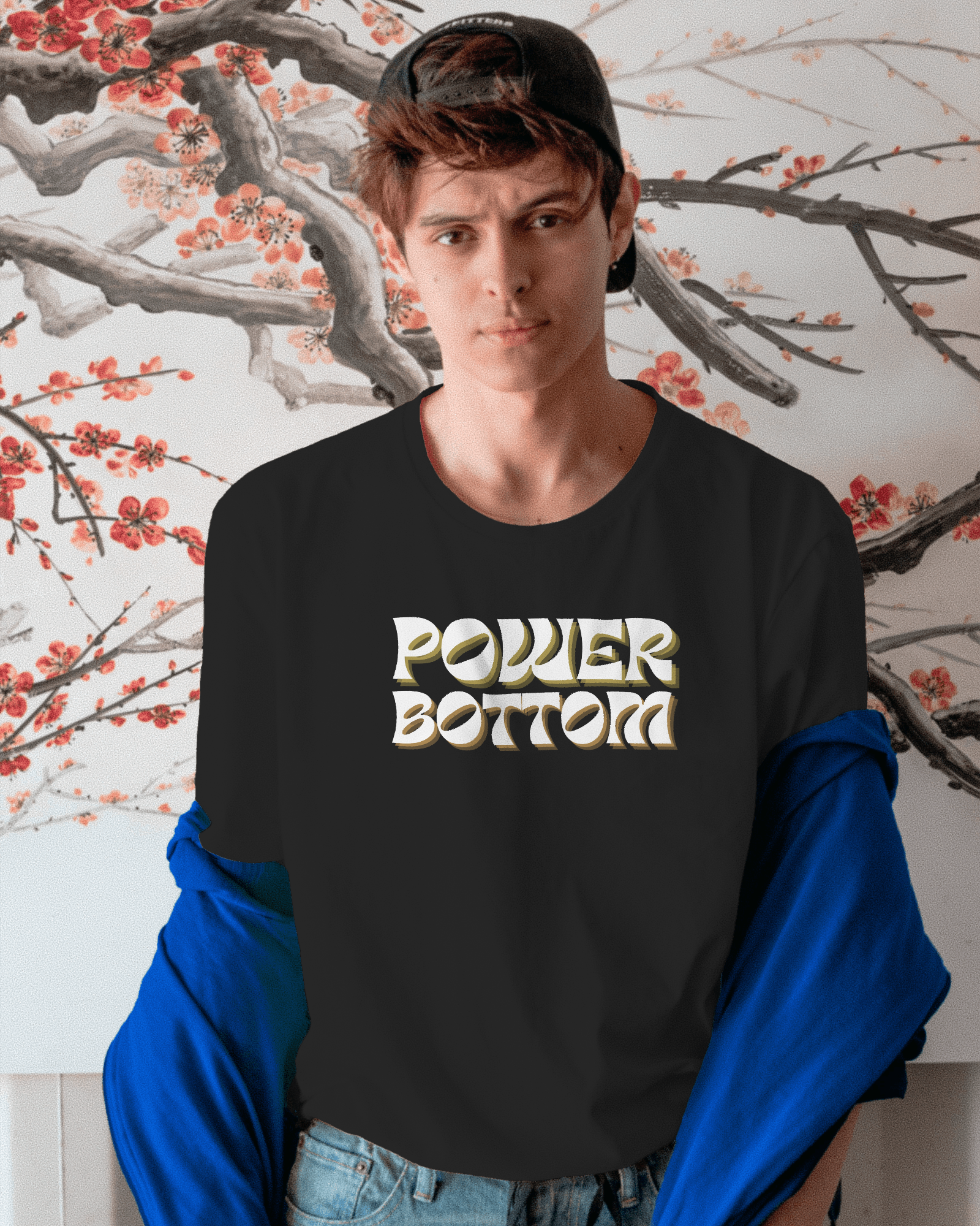 Person wearing a black sweatshirt with 'POWER BOTTOM' text in front of a floral wall.Kink, LGBTQIA+, Queer Sub Dom 