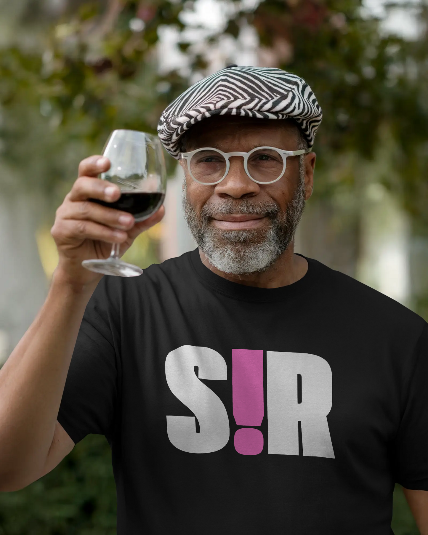 Man holding a glass of red wine outdoors wearing a black t-shirt with 'S!R' text.  Kink, LGBTQIA+, Queer Sub Dom