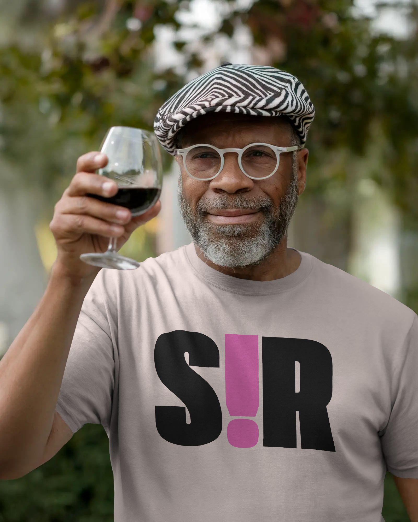 Man holding a glass of red wine outdoors wearing a t-shirt with 'S!R' design. Kink, LGBTQIA+, Queer Sub Dom