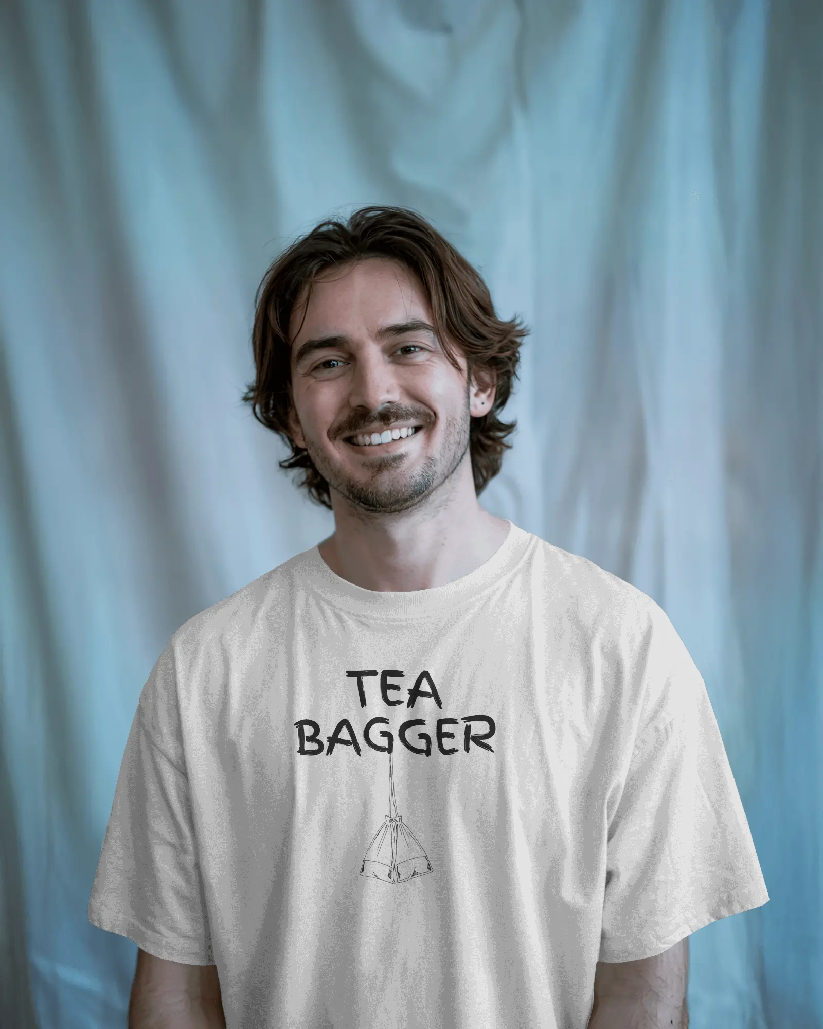 Man wearing a 'TEA BAGGER' t-shirt against a light blue curtain background   Kink, LGBTQIA+, Queer
