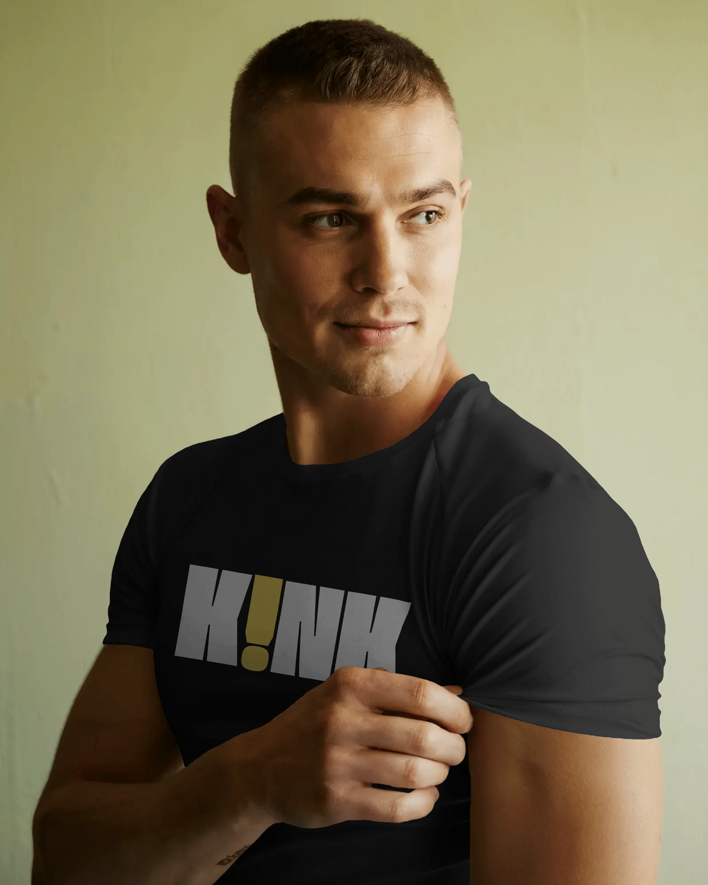 Man wearing a black t-shirt with 'KINK' printed on it against a plain background  Kink, LGBTQIA+, Queer