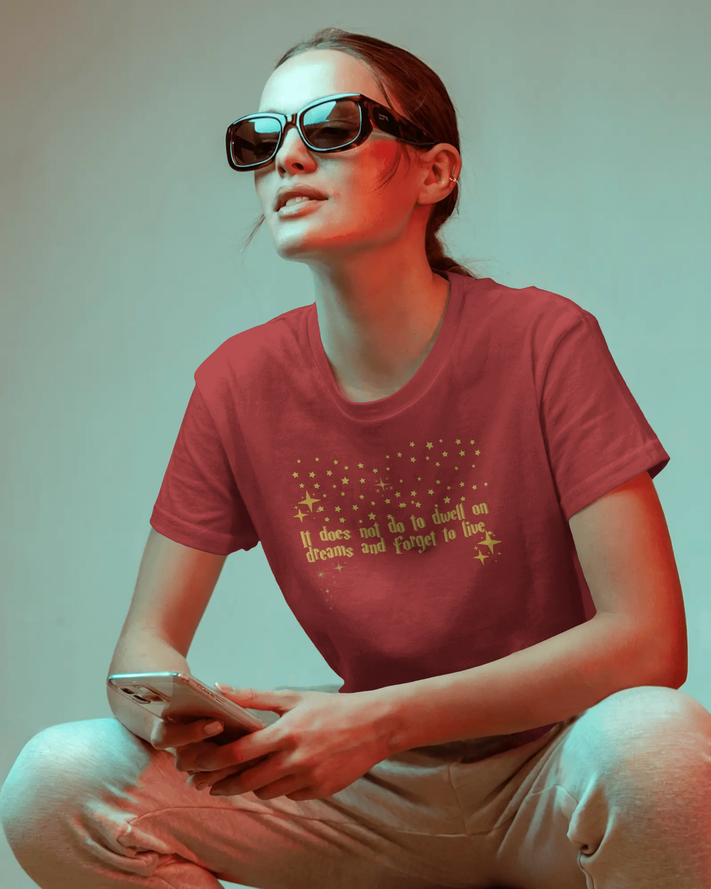 Person wearing a red t-shirt with text, sitting and holding a phone against a plain background, Dumbledore quote, harry potter