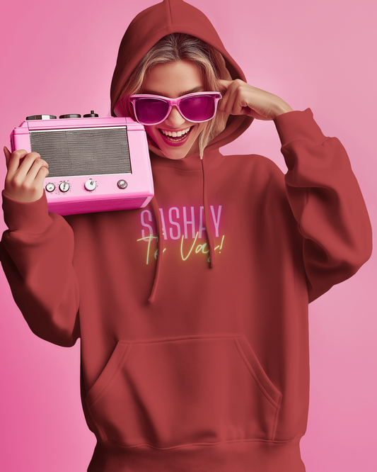 Person wearing a red hoodie with text, holding a pink vintage-style radio against a pink background  Drag Race Espana, Drag Race Spain, Rupaul's drag race, Drag queens, LGBT, Queer culture