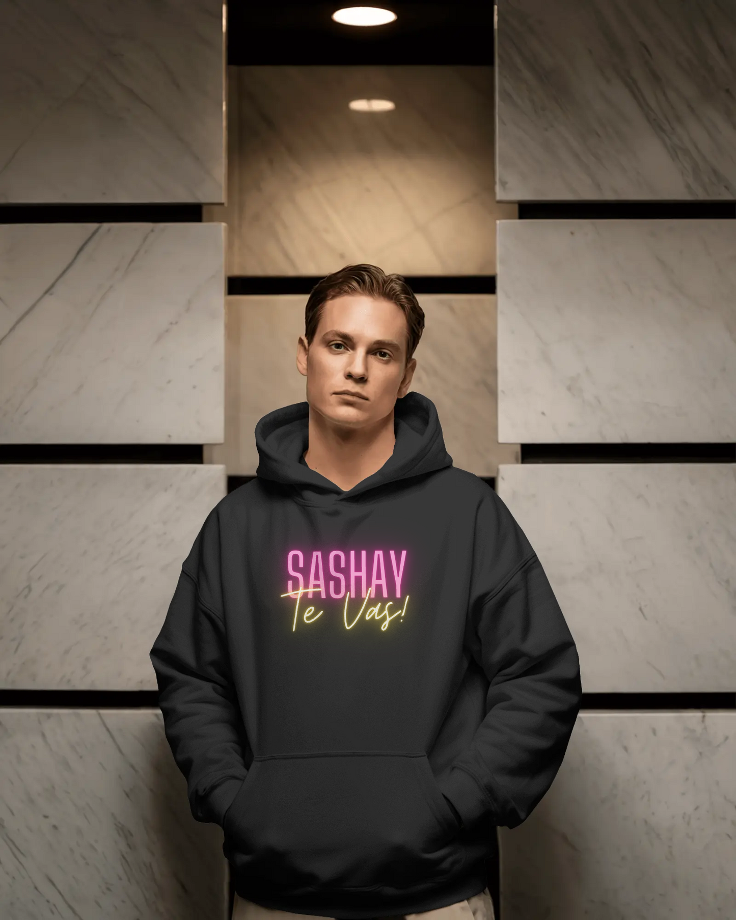 Person wearing a black hoodie with 'SASHAY Te Vas!' text in pink and yellow against a geometric wall.  Drag Race Espana, Drag Race Spain, Rupaul's drag race, Drag queens, LGBT, Queer culture