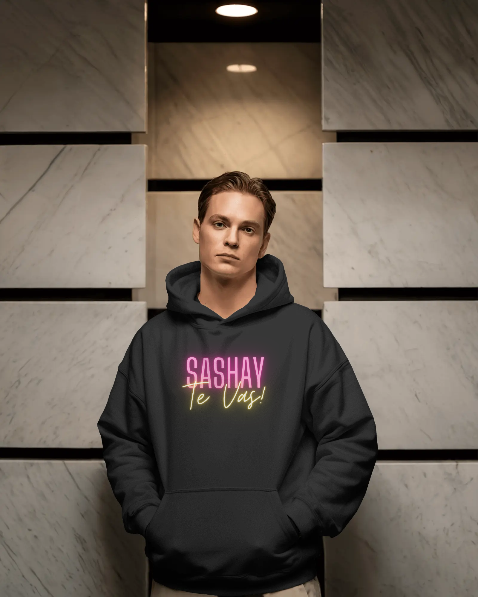Person wearing a black hoodie with 'SASHAY Te Vas!' text in pink and yellow against a geometric wall.  Drag Race Espana, Drag Race Spain, Rupaul's drag race, Drag queens, LGBT, Queer culture