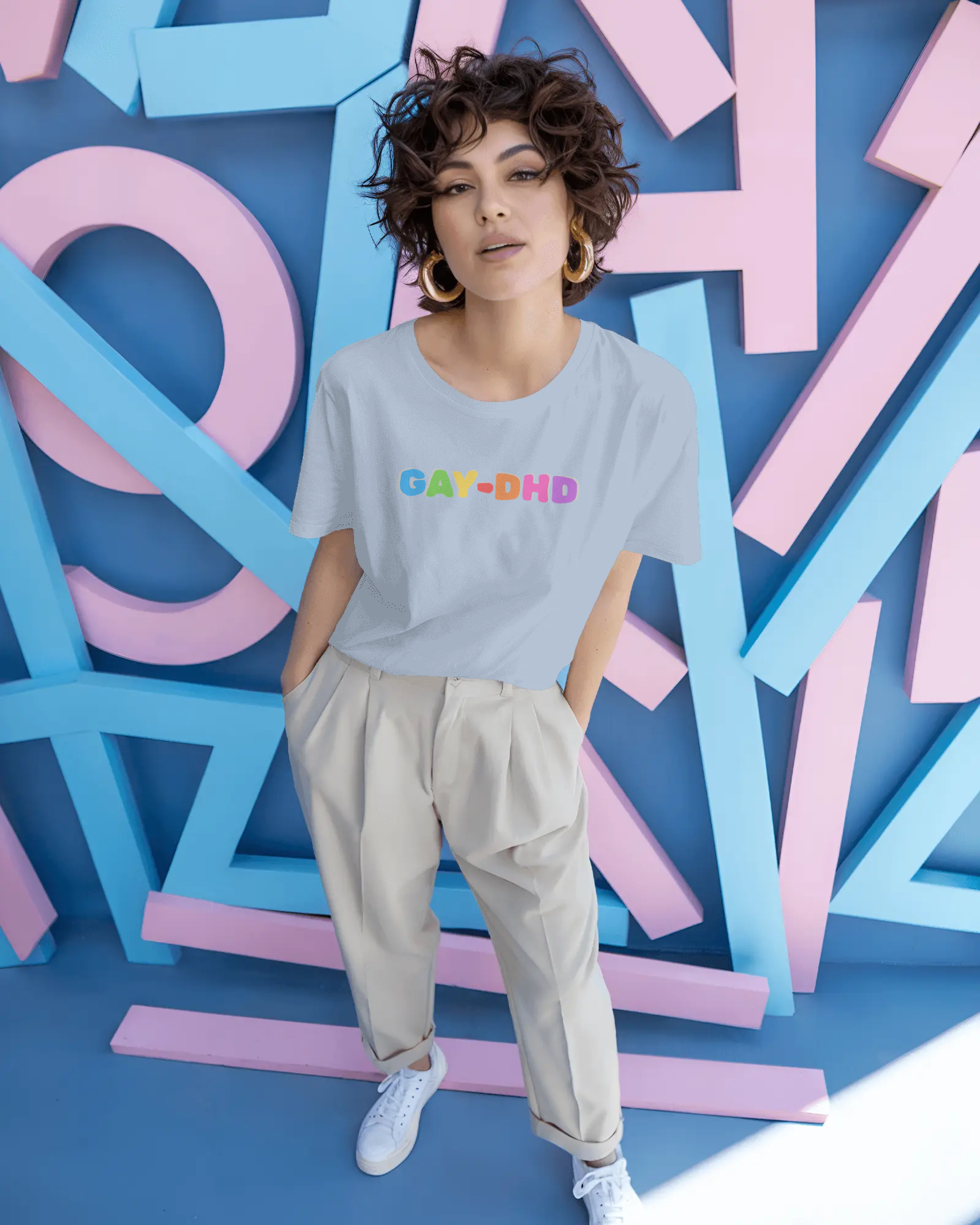 Person wearing a light gray t-shirt with colorful text in front of a colorful geometric background