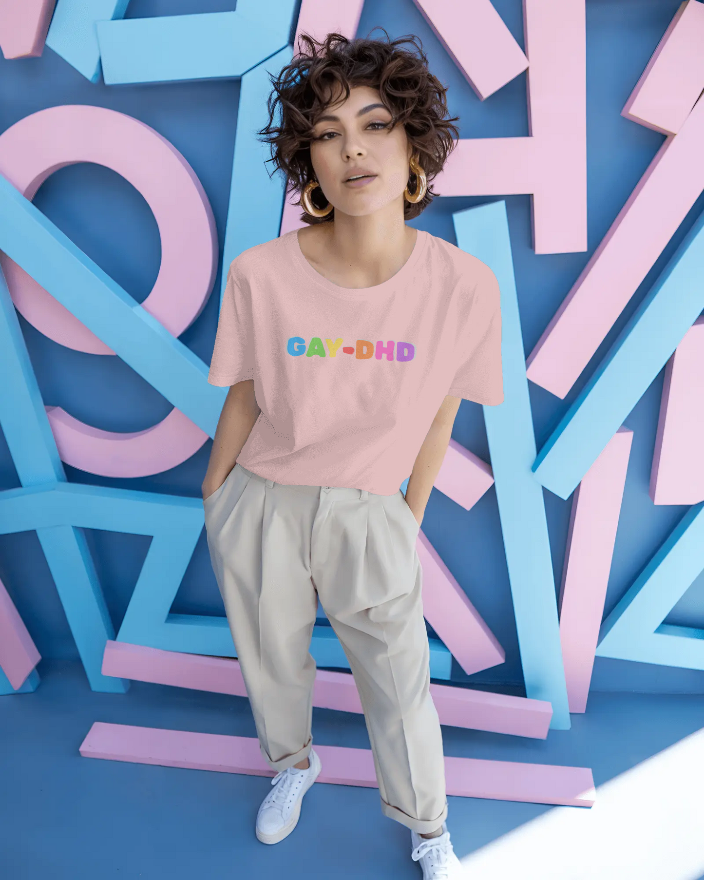 Person wearing a pink t-shirt with 'GAY-DHD' text in colorful letters against a vibrant, abstract background.