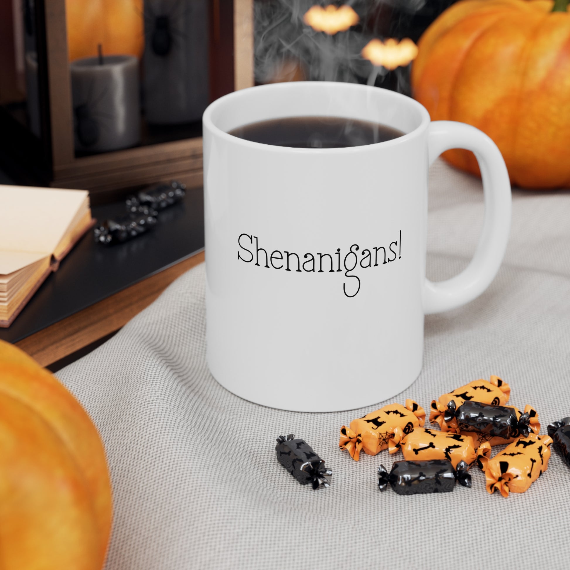 White mug with 'Shenanigans!' text, surrounded by Halloween-themed treats and pumpkins.