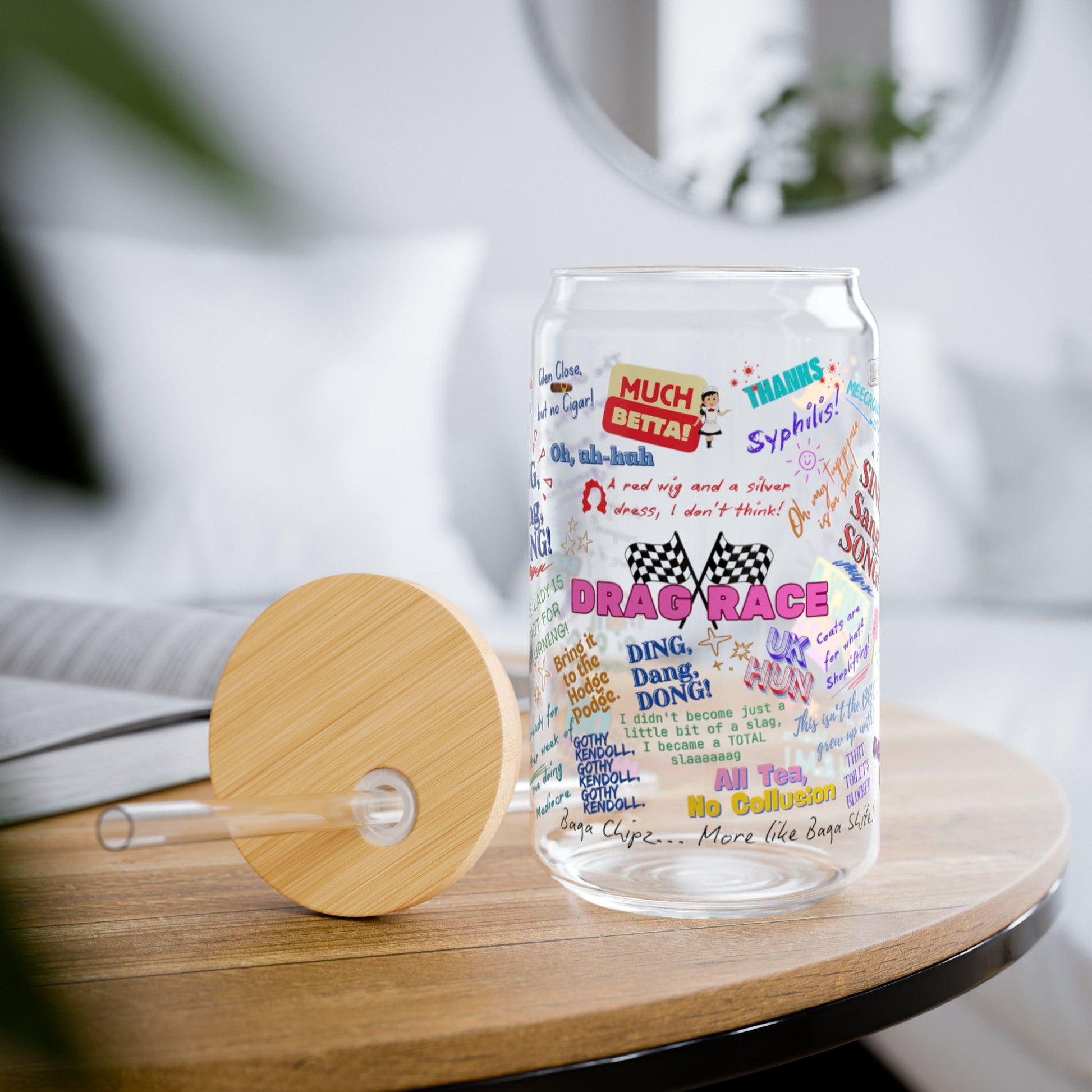 Clear glass tumbler with colorful text design on a wooden table Features iconic Quotes from your favorite Drag Race UK  Drag Queens.