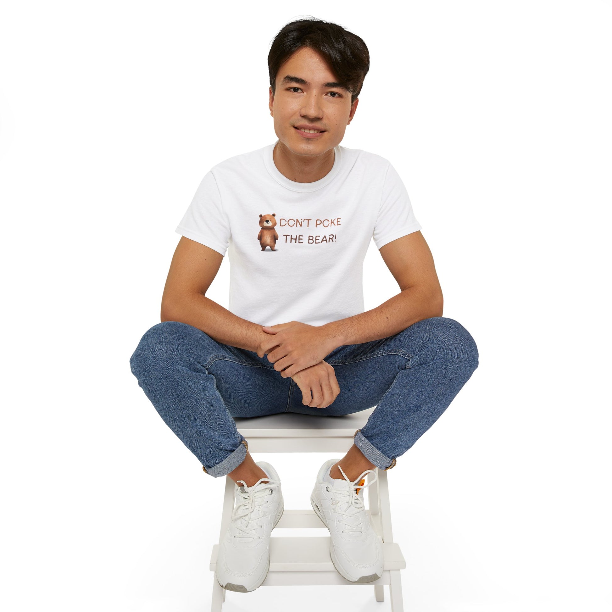 Person wearing a white t-shirt with a graphic and text, sitting on a white stool against a white background
