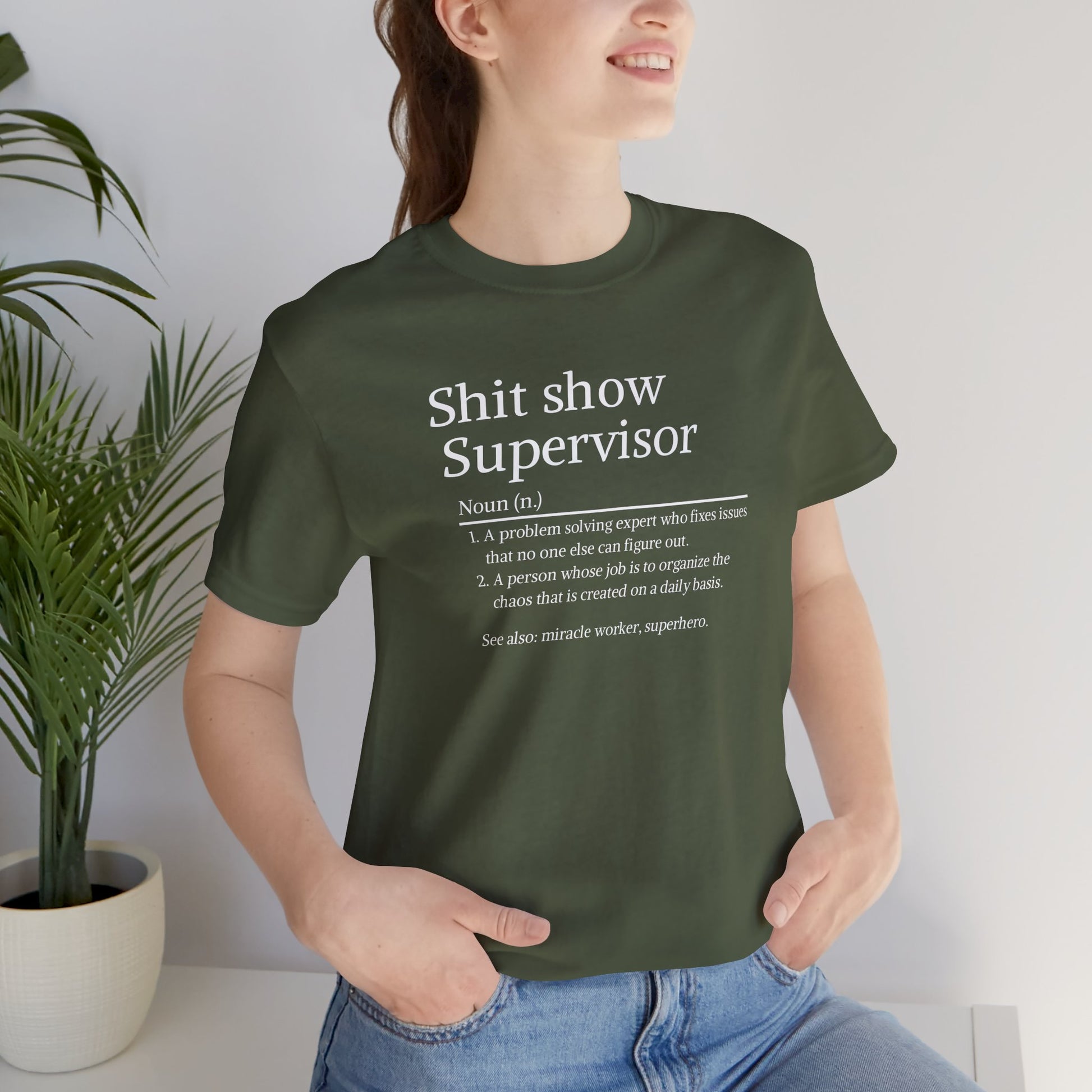 Person wearing a green t-shirt with text, standing indoors next to a plant.