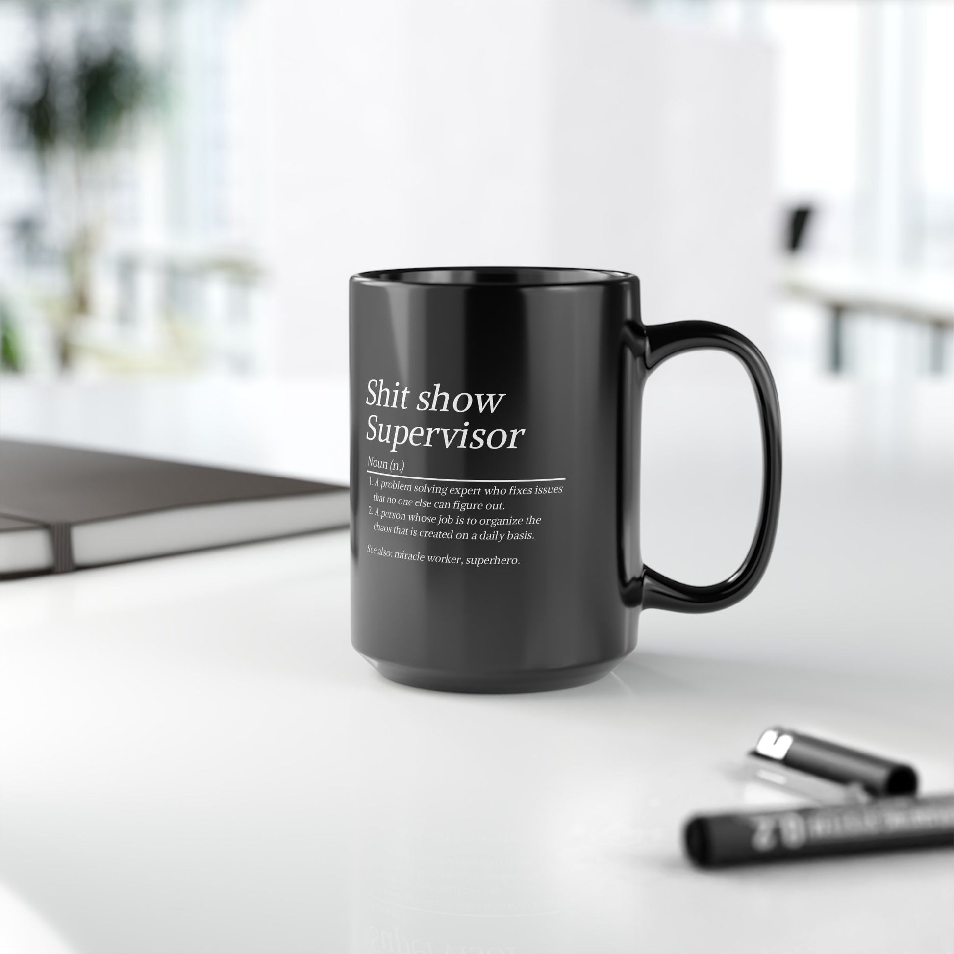 Black mug with text on a white surface with office items in the background