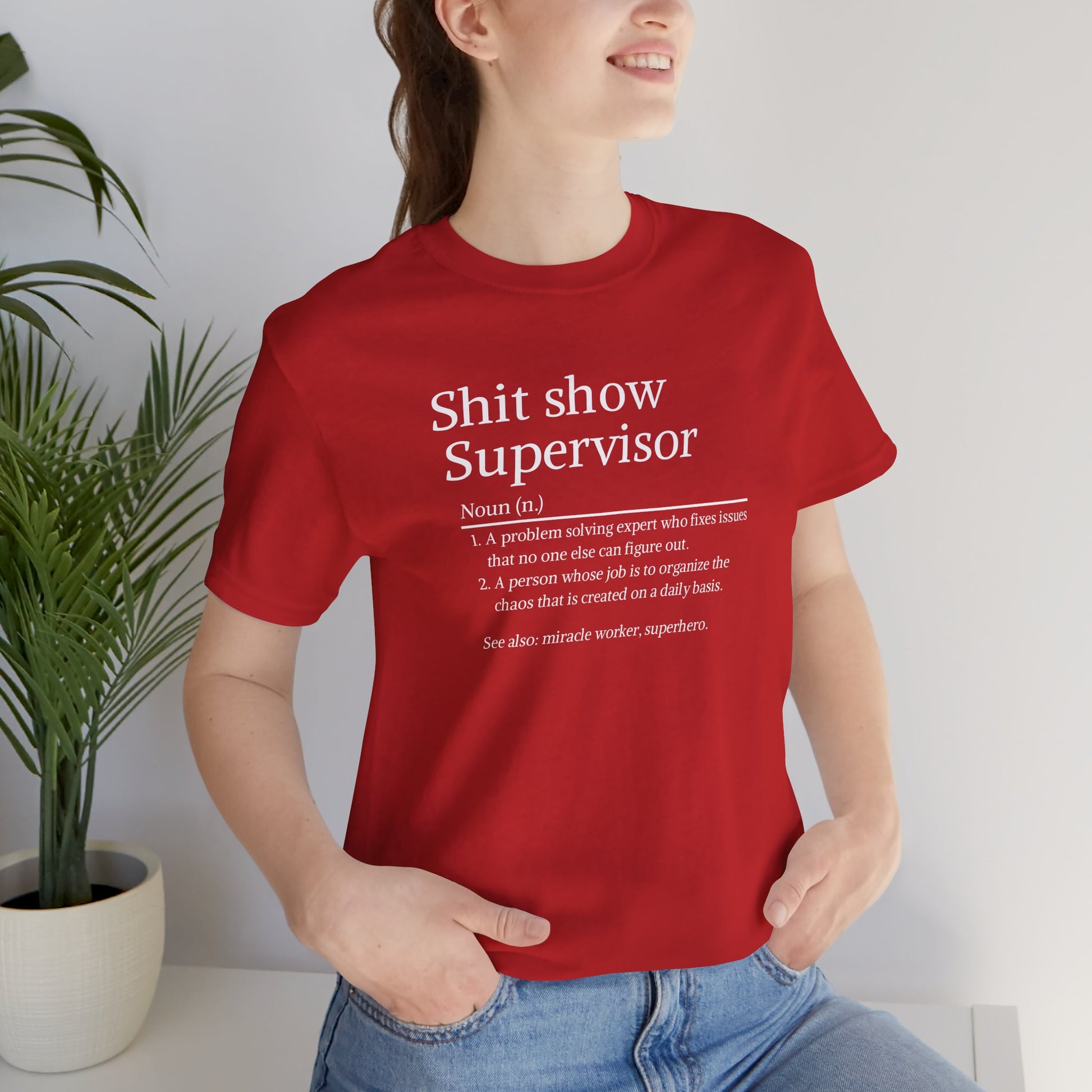 Person wearing a red t-shirt with text, standing indoors next to a plant.