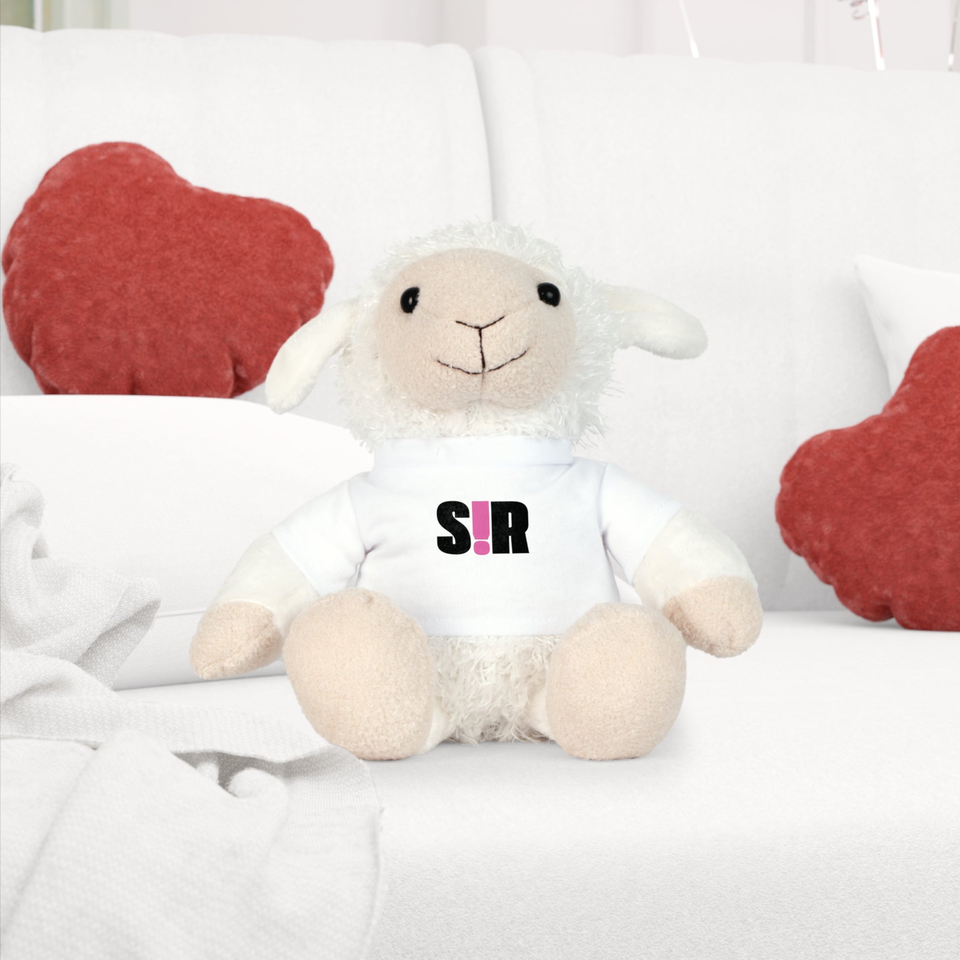 White plush lamb toy with 'SIR' logo on a white couch with red heart cushions.